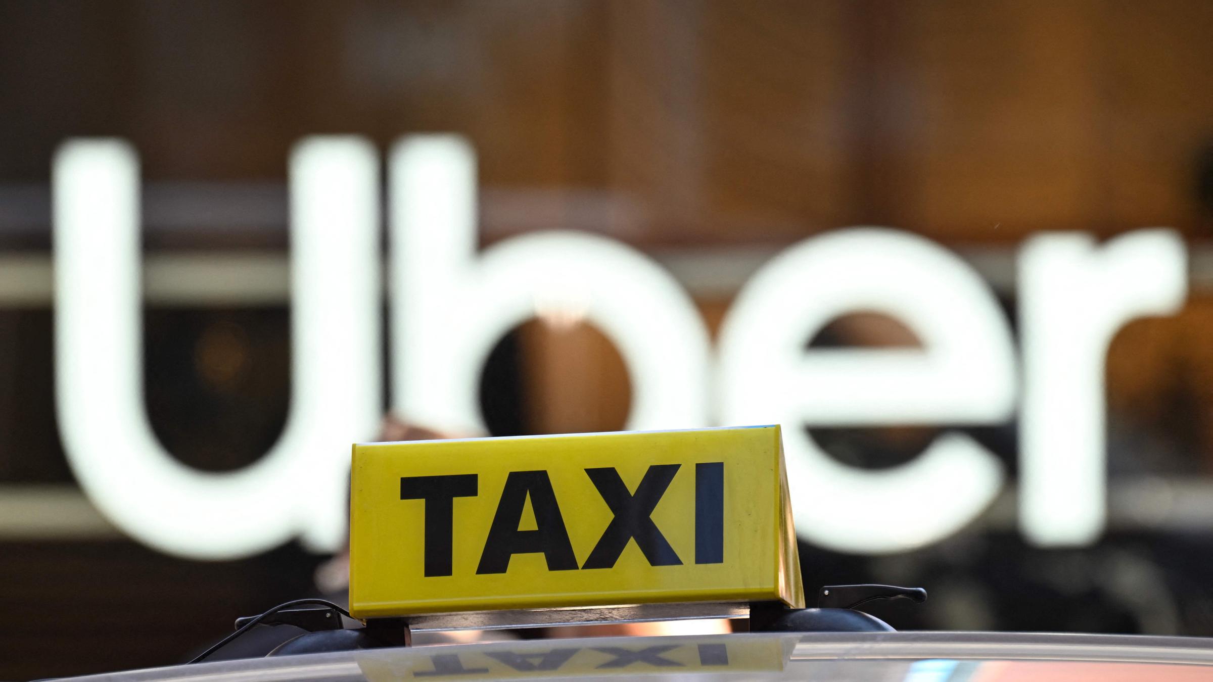 Logo eines Taxis auf einem Autodach vor dem Logo von Uber im Hintergrund