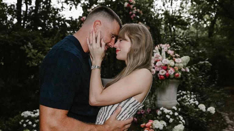 Taylor Swift und Travis Kelce eng umschlungen im Garten mit vielen Blumen im Hintergrund: offizielles Verlobungsfoto