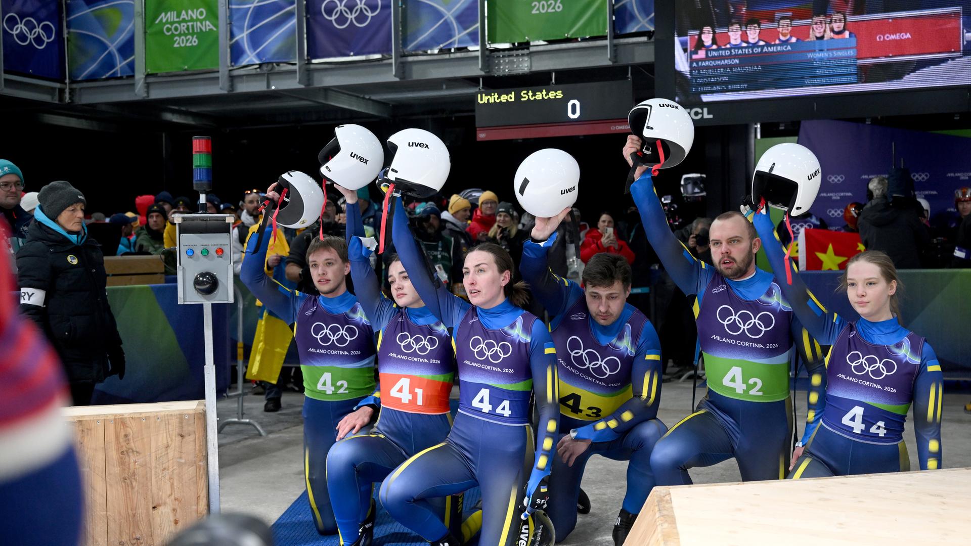 Das Team der Ukraine kniet am Boden und hebt im Zielbereich gemeinsam die Helme nach oben.