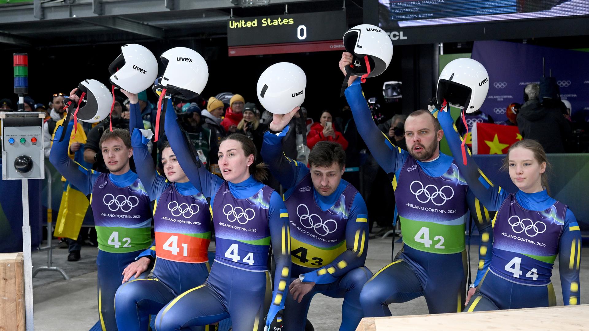 Das Team der Ukraine kniet am Boden und hebt im Zielbereich gemeinsam die Helme nach oben.