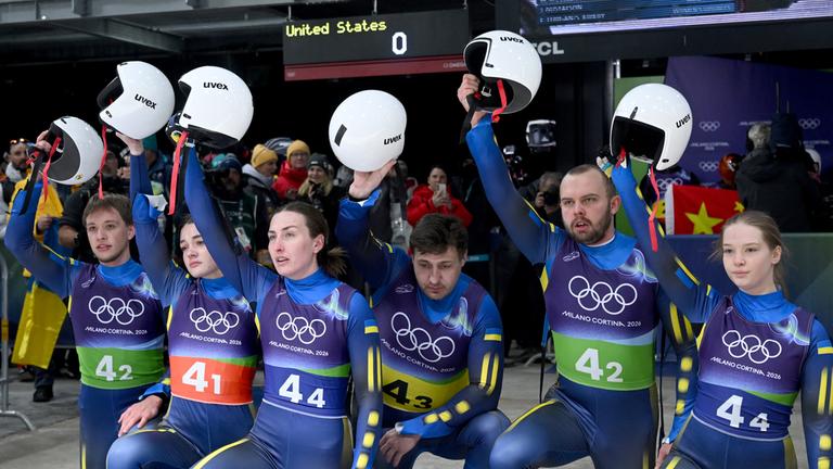 Das Team der Ukraine kniet am Boden und hebt im Zielbereich gemeinsam die Helme nach oben.