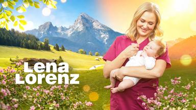 Hebamme Lena Lorenz (Judith Hoersch) steht vor der sonnigen Bergkulisse des Watzmann in den österreichischen Alpen. Sie hält ein Baby im Arm und schaut es liebevoll an.
