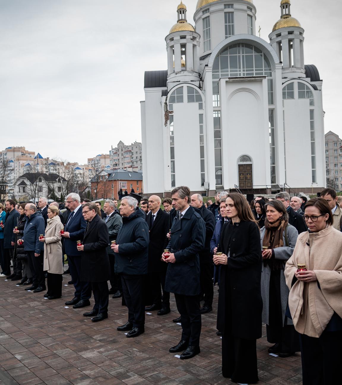 Man sieht eine Gedenkzeremonie in Butscha, im Hintergrund eine weiße Kirche.