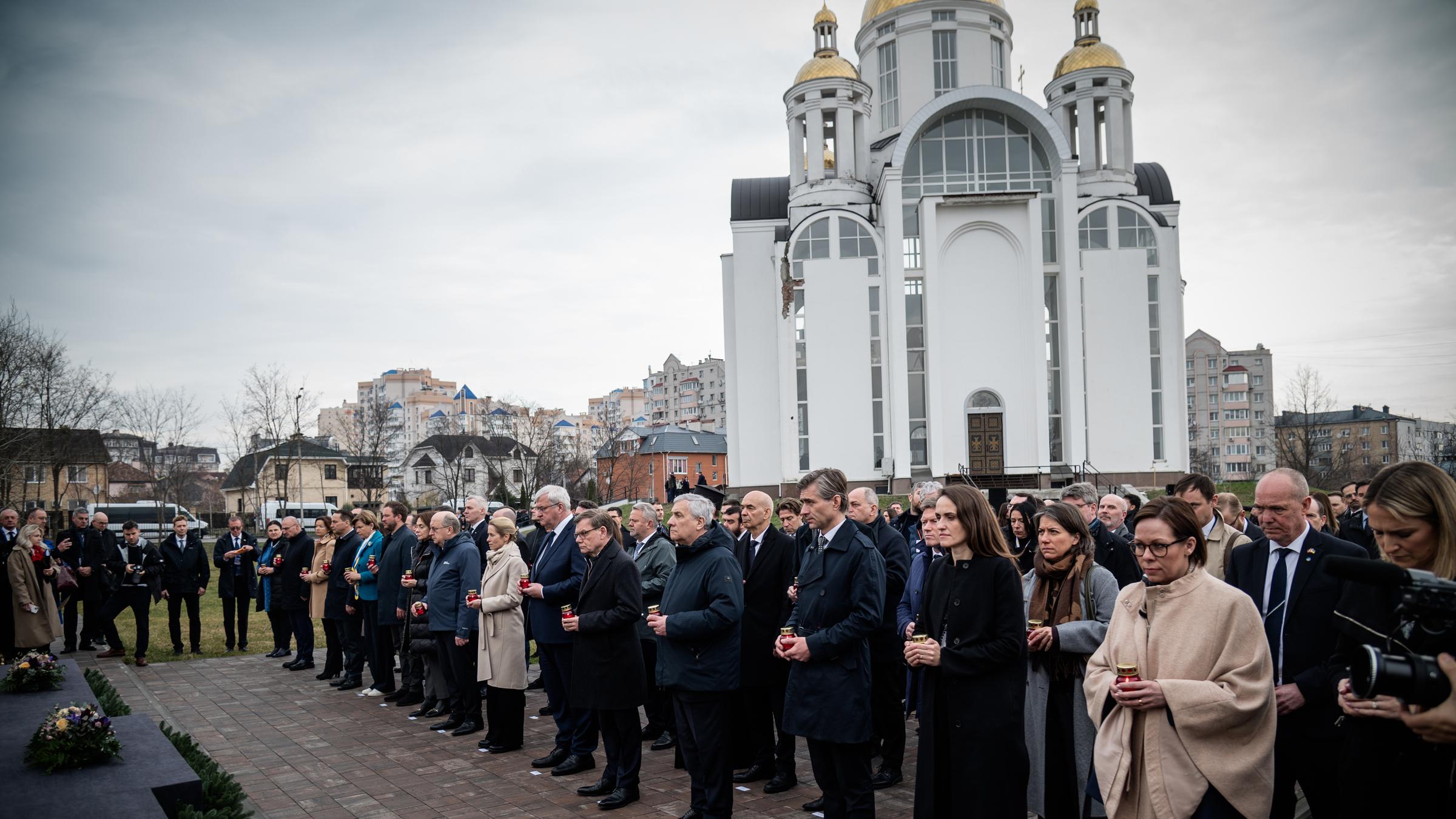 Man sieht eine Gedenkzeremonie in Butscha, im Hintergrund eine weiße Kirche.
