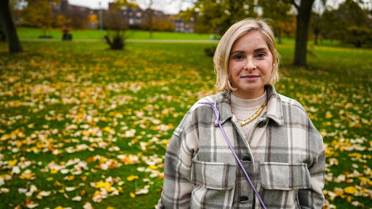 Junge Frau mit blonden Haaren steht auf einer Herbstwiese.