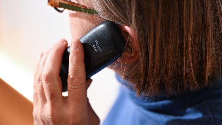 Eine Frau mit Brille telefoniert am Festnetztelefon. 