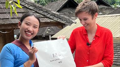 Xian Jin steht neben Miriam Steimer und sie halten gemeinsam ein Papier hoch.