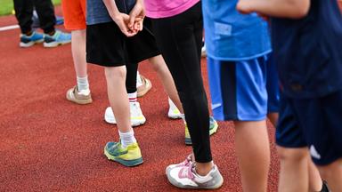 Symbolbild: Kinder einer Grundschule stehen im Rahmen der Bundesjugendspiele auf einem Sportplatz.