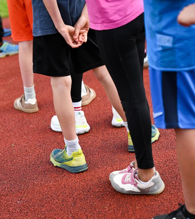 Symbolbild: Kinder einer Grundschule stehen im Rahmen der Bundesjugendspiele auf einem Sportplatz.