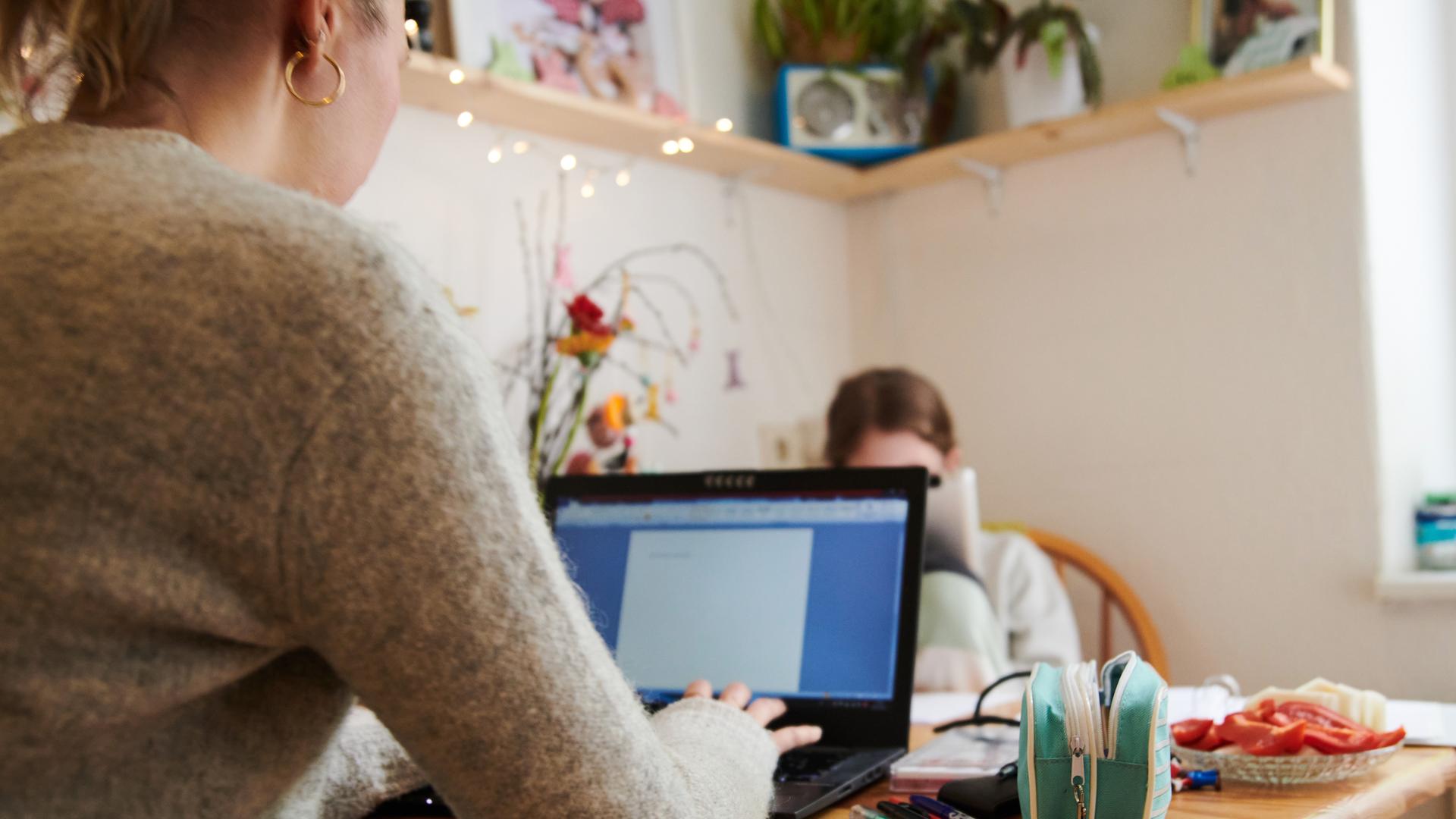 29.04.2021, Berlin: Eine Mutter arbeitet am Küchentisch während ihre Tochter gegenüber in ein Tablet guckt.