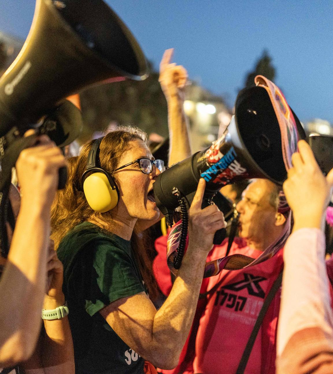 Israelische Aktivisten bei einer Demonstration gegen den andauernden Krieg mit dem Iran, eine Frau ruft etwas in ein Megafon.