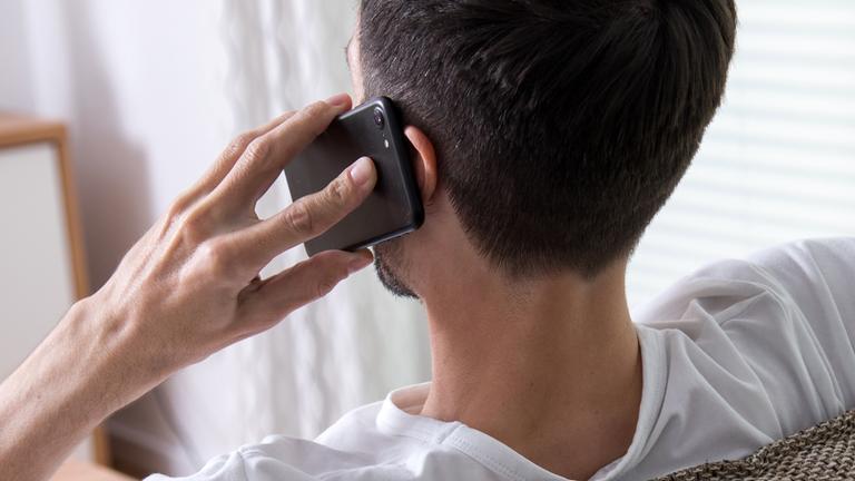 Ein Mann hält sich ein Handy ans Ohr und man schaut ihm über die Schulter.