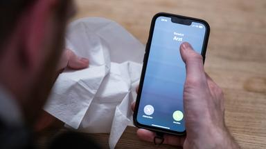 Symbolbild: Ein Mann mit Taschentuch in der Hand ruft via Smartphone beim Arzt an