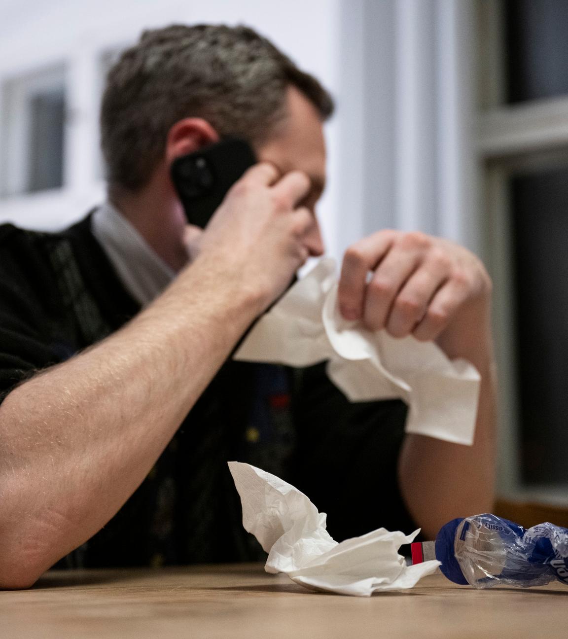 Ein Mann hält ein Taschentuch in einer Hand und ein Telefon in der Anderen.