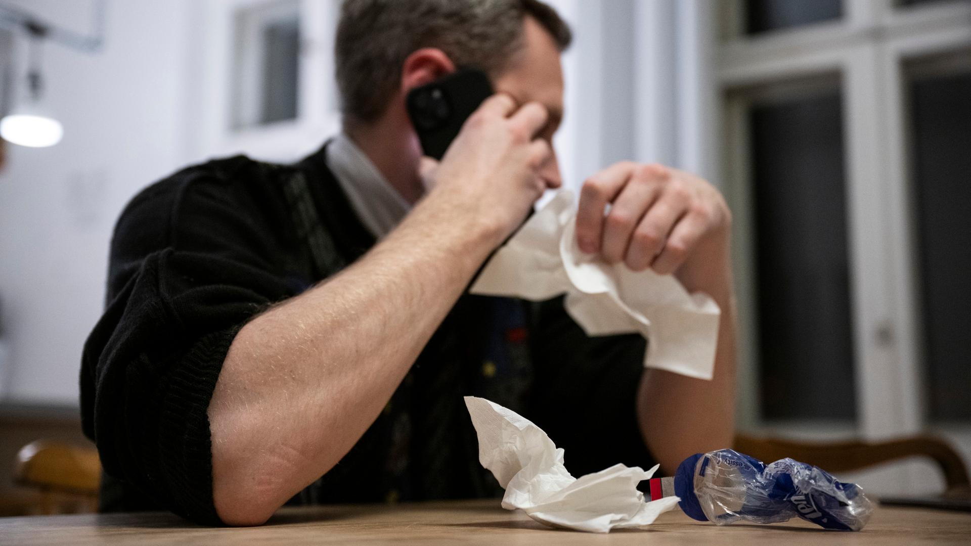 Ein Mann hält ein Taschentuch in einer Hand und ein Telefon in der Anderen.