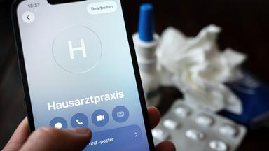 Eine Person hält ein Smartphone in der Hand und ruft eine Hausarztpraxis an. 