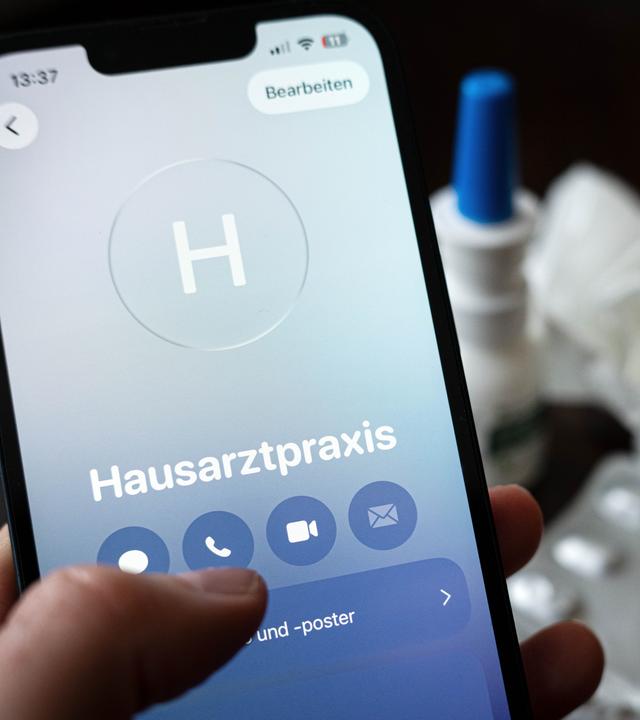 Eine Person hält ein Smartphone in der Hand und ruft eine Hausarztpraxis an. 