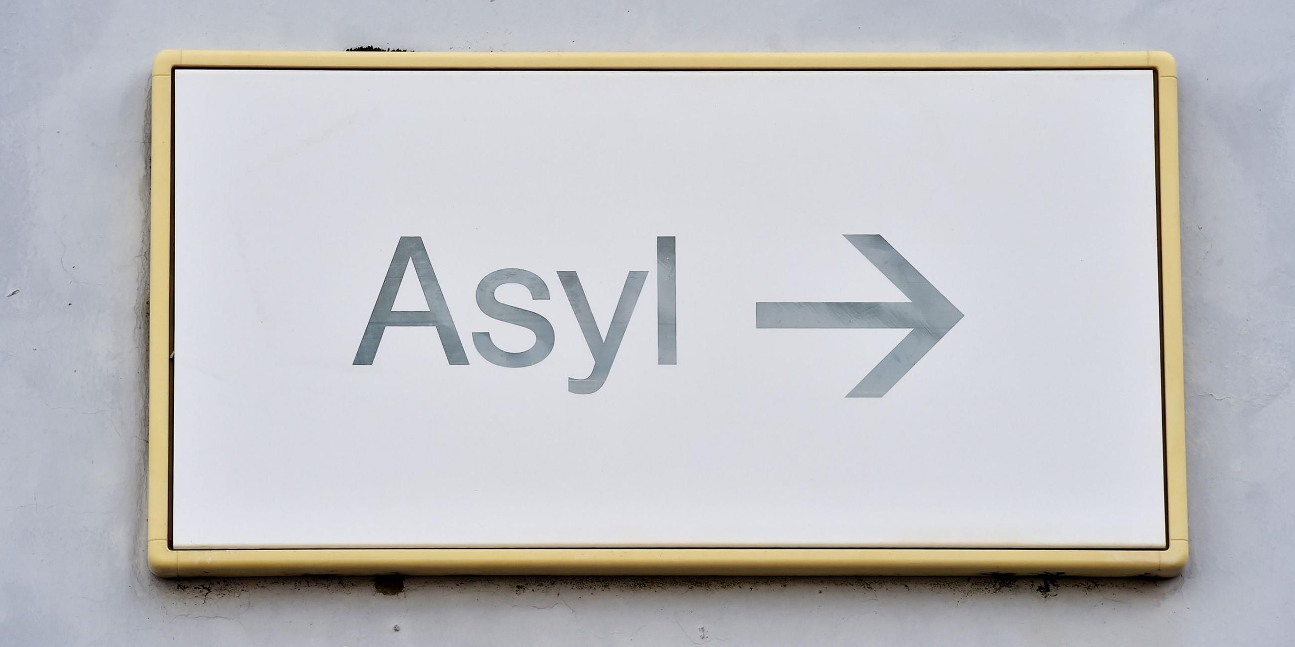 Auf einem Schild "Asyl" weist ein Pfeil Flüchtlingen den Weg zur Stelle für Asylanträge.