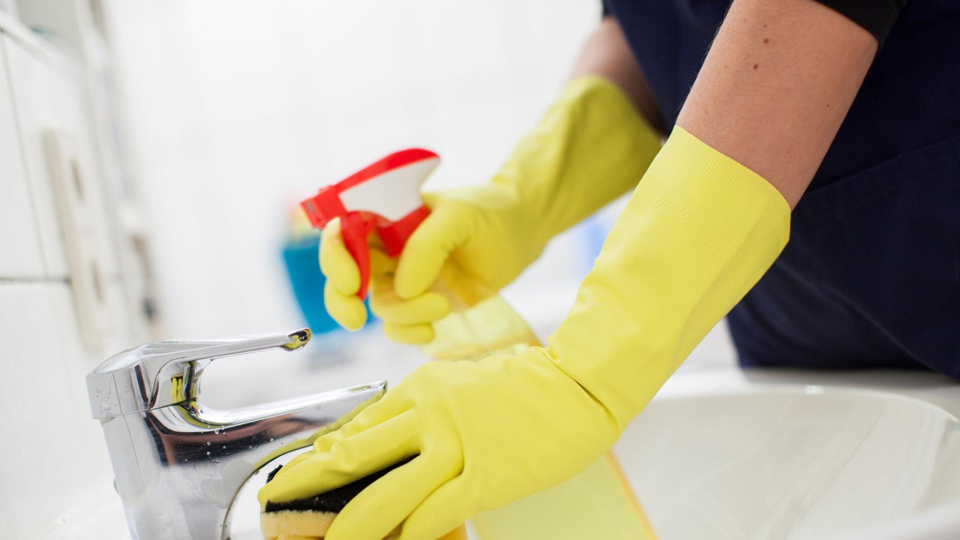 Eine Haushaltshilfe putzt das Waschbecken. Symbolbild