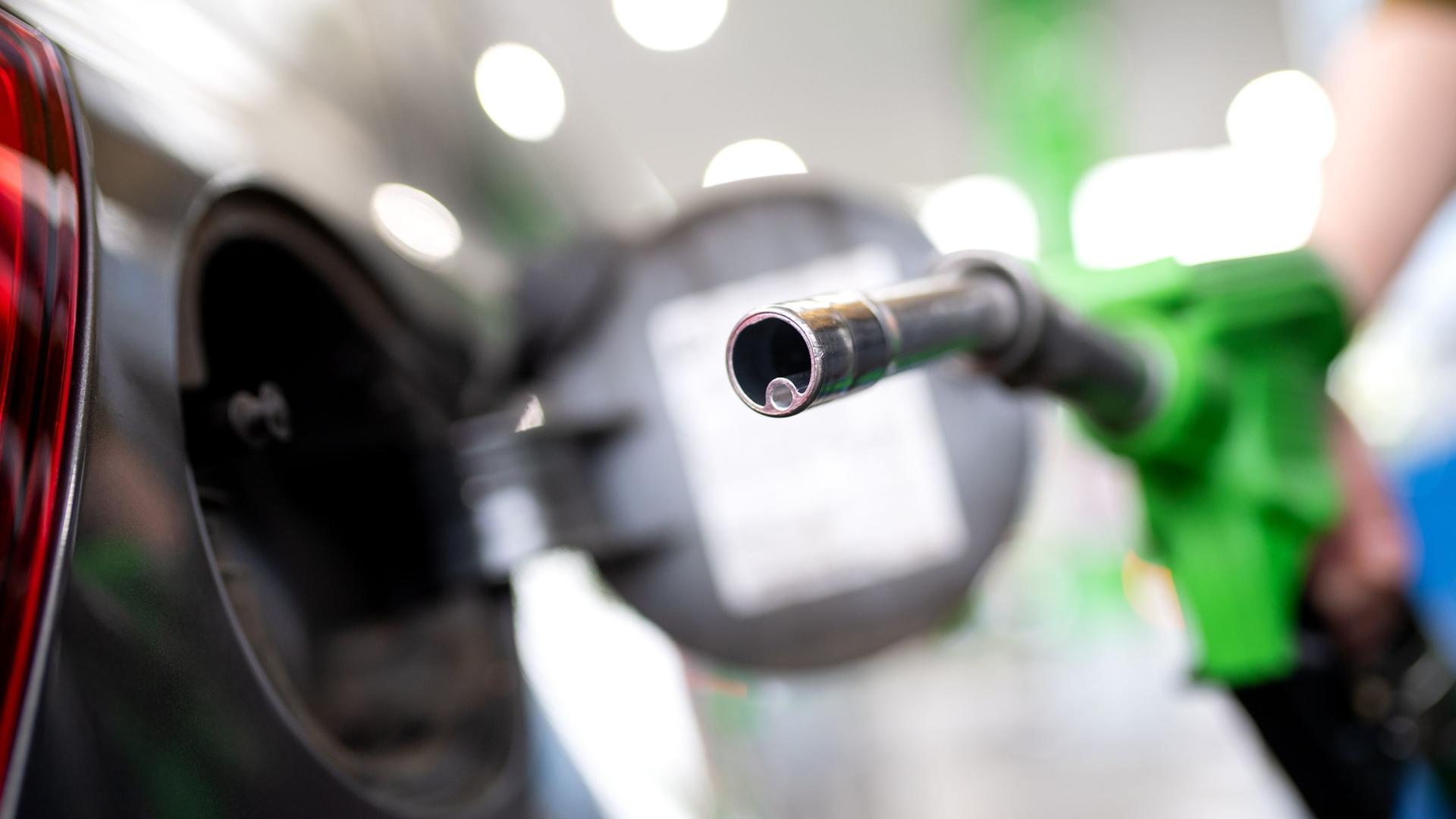 Frau hält an einer Tankstelle eine Zapfpistole. Symbolpolitik