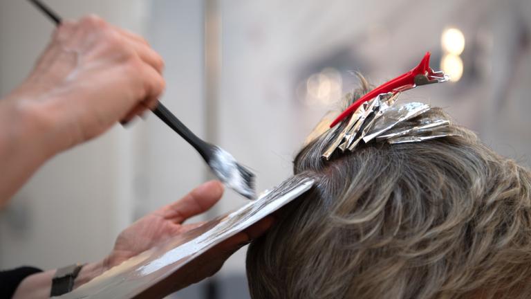 Friseurin färbt einer Kundin mit einem Pinsel die Haare. Symbol