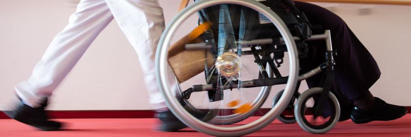 Pfleger schiebt einen Rollstuhl in einem Pflegeheim.