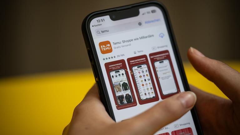Eine Person hält ein Handy mit der App Temu in den Händen. 
