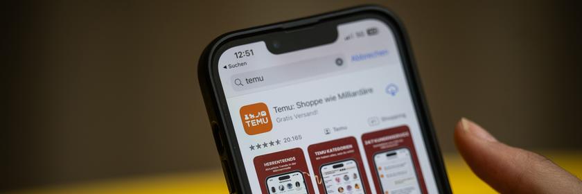 Eine Person hält ein Handy mit der App Temu in den Händen. 