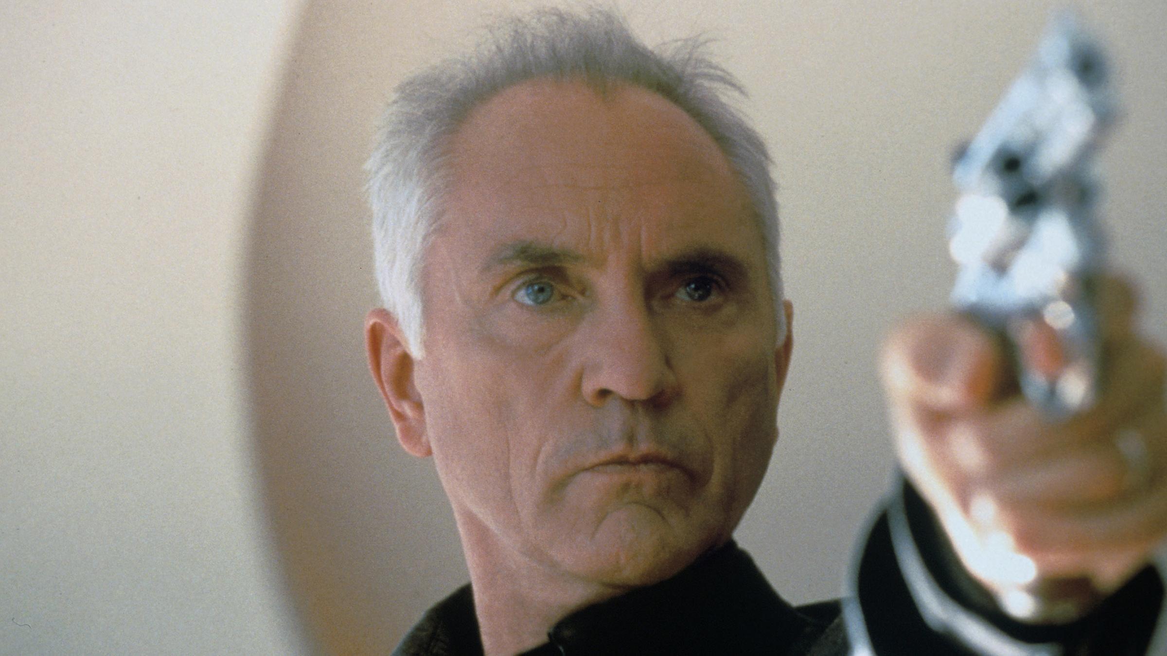 Terence Stamp in einer Filmrolle, wie er eine Waffe hält.