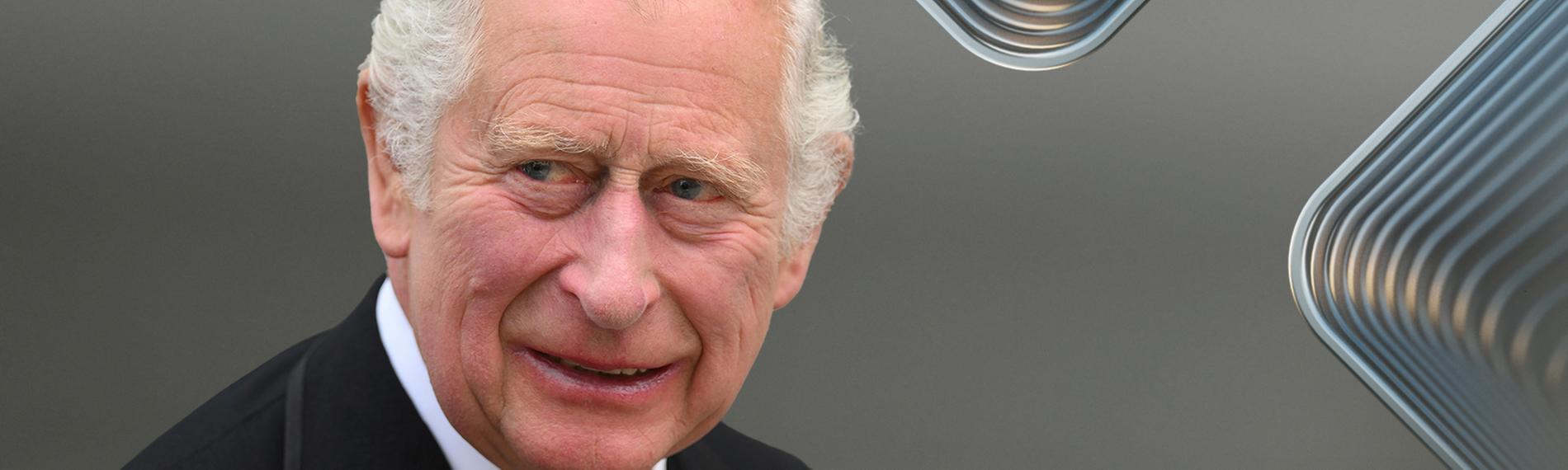 König Charles III. blickt vor unscharfem Hintergrund zur Seite und lächelt in die Kamera.