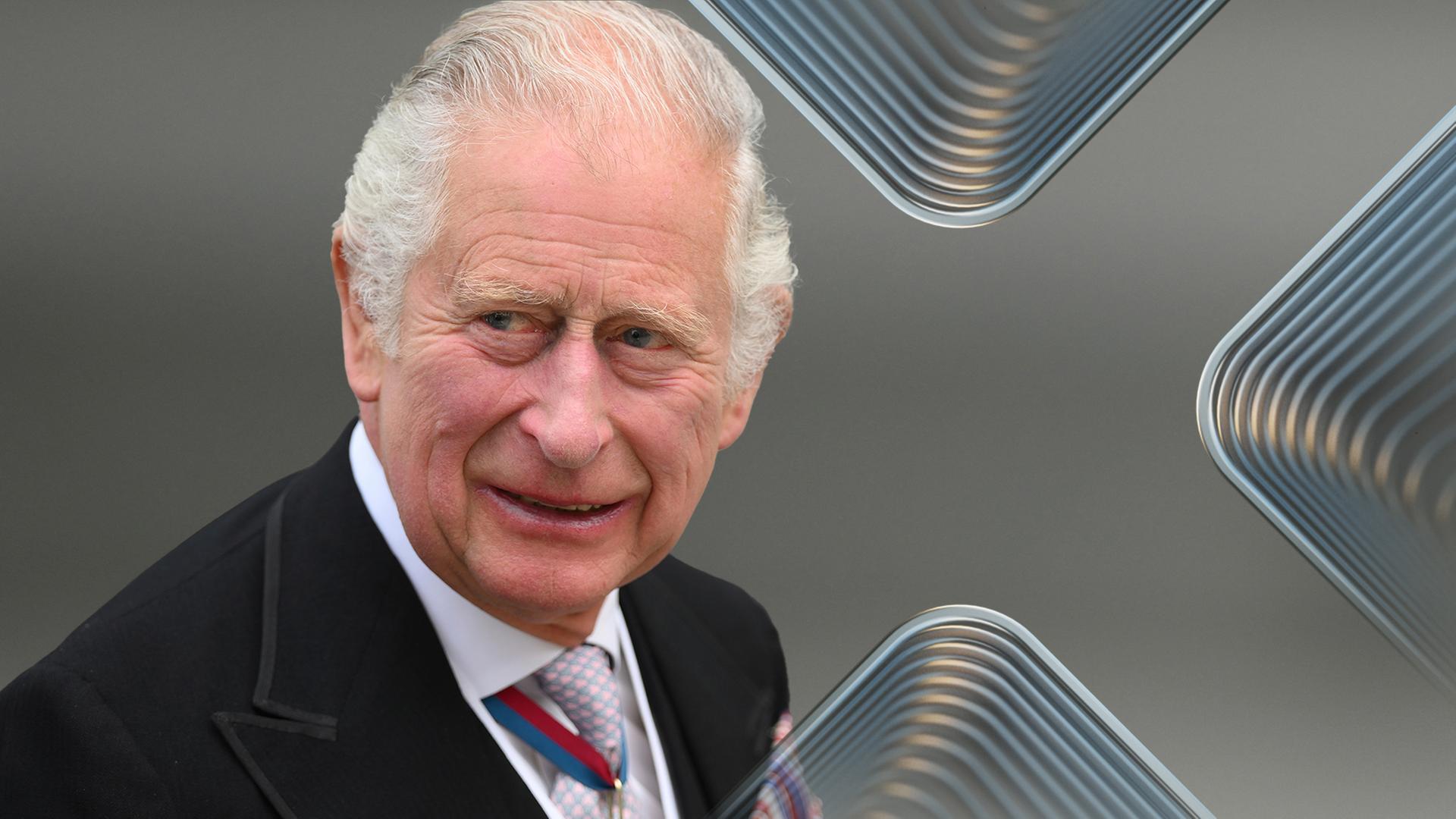 König Charles III. blickt vor unscharfem Hintergrund zur Seite und lächelt in die Kamera.