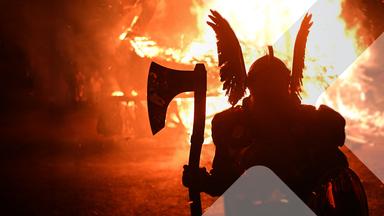 Eine als Wikinger verkleidete Person vor einem großen Feuer. 