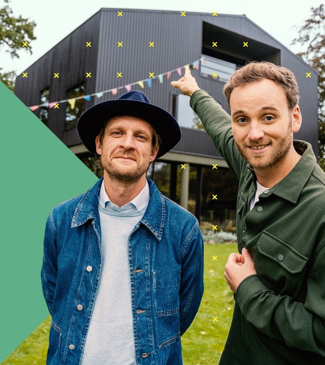 Leon Windscheid steht neben einem Mann in Jeansjacke und Hut und zeigt auf ein Haus.