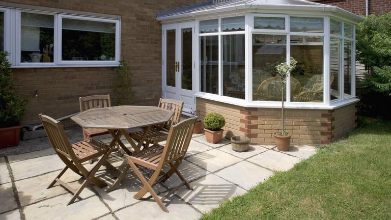 Eine Terrasse mit Tisch und Stühlen befindet sich vor einem Haus mit Wintergarten.