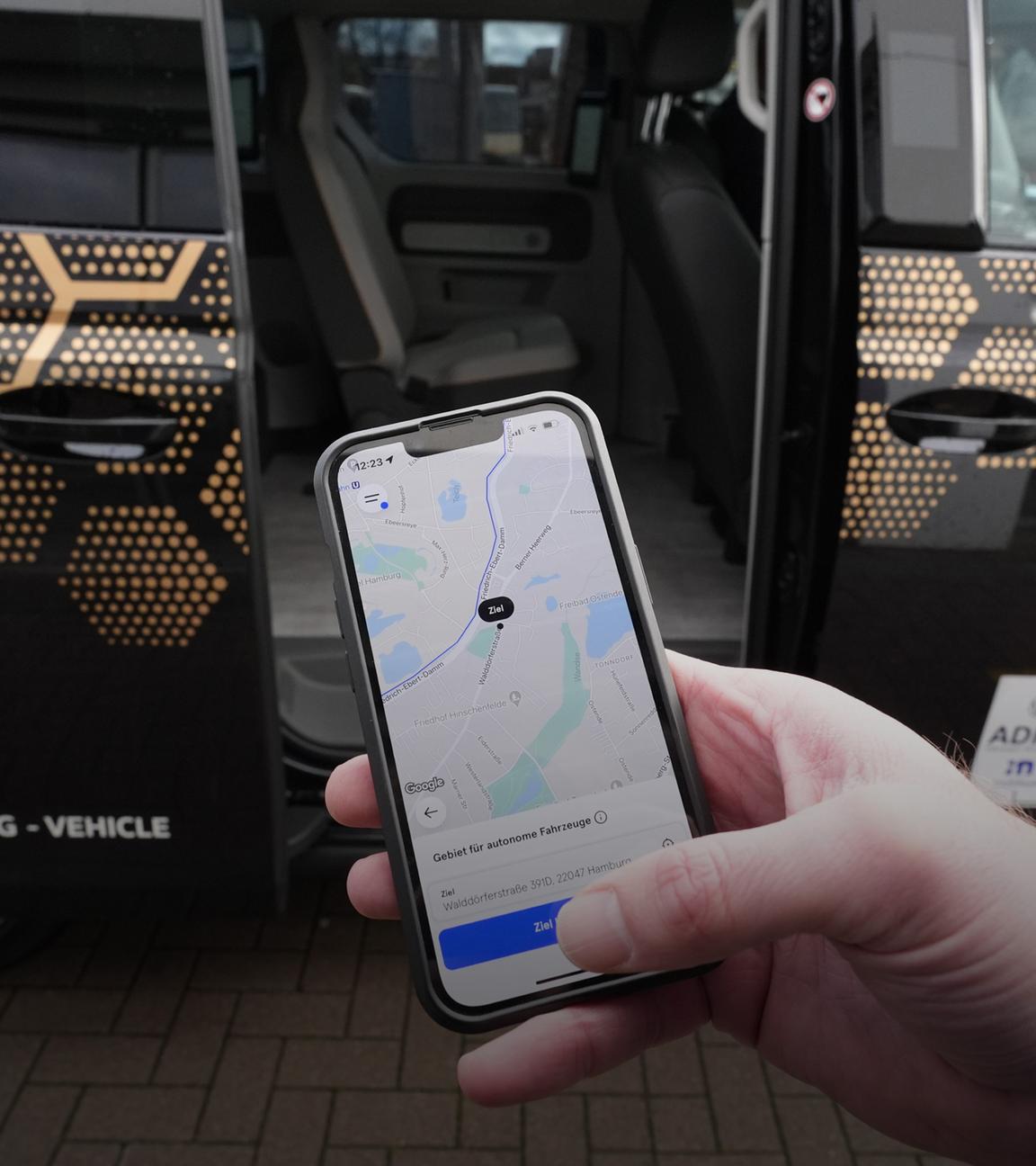Hamburg: Ein Mitarbeiter hält ein Smartphone mit der Moia-App vor einen autonom fahrenden ID. Buzz AD von Volkswagen (gestellte Szene).