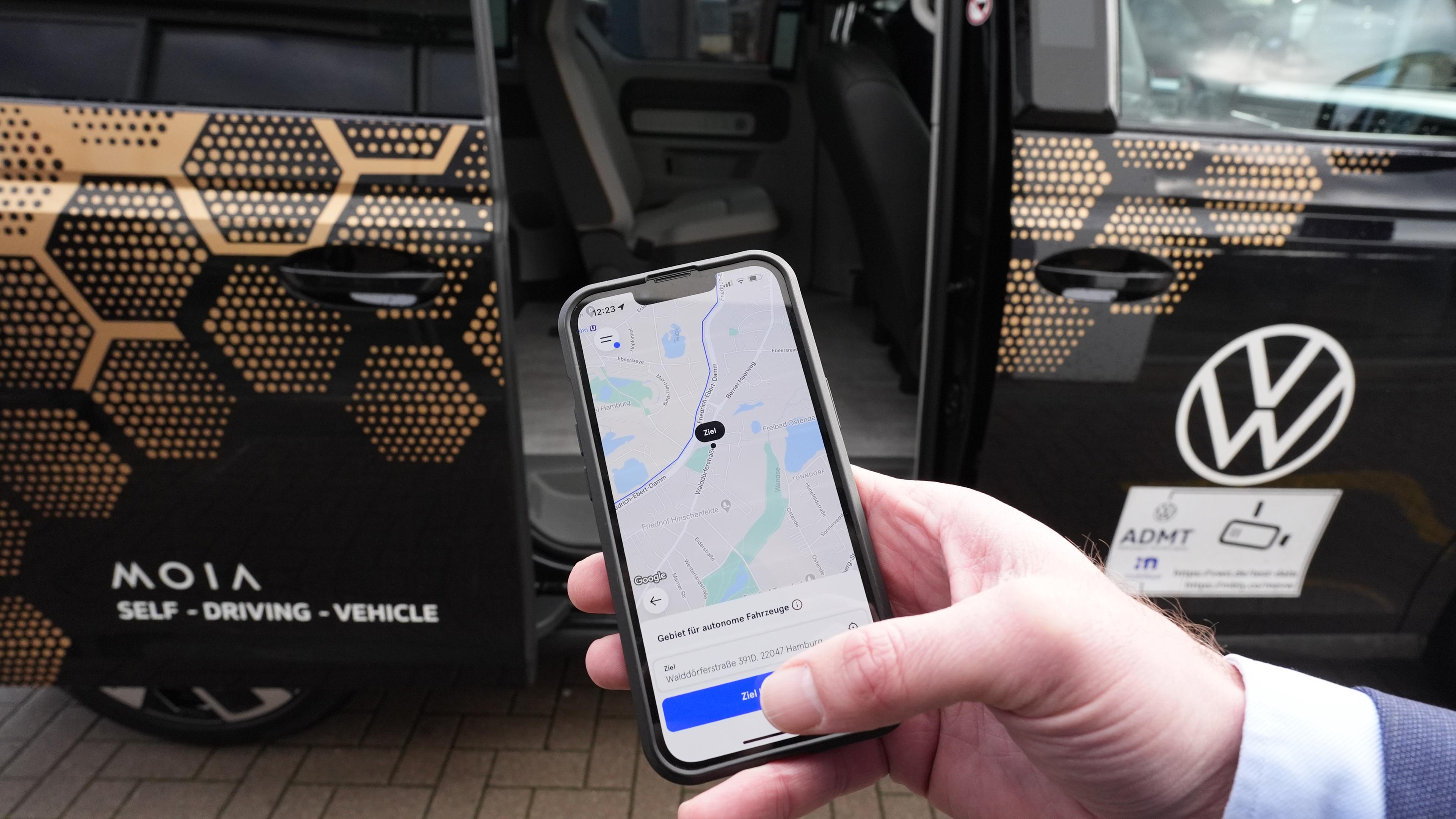 Hamburg: Ein Mitarbeiter hält ein Smartphone mit der Moia-App vor einen autonom fahrenden ID. Buzz AD von Volkswagen (gestellte Szene).