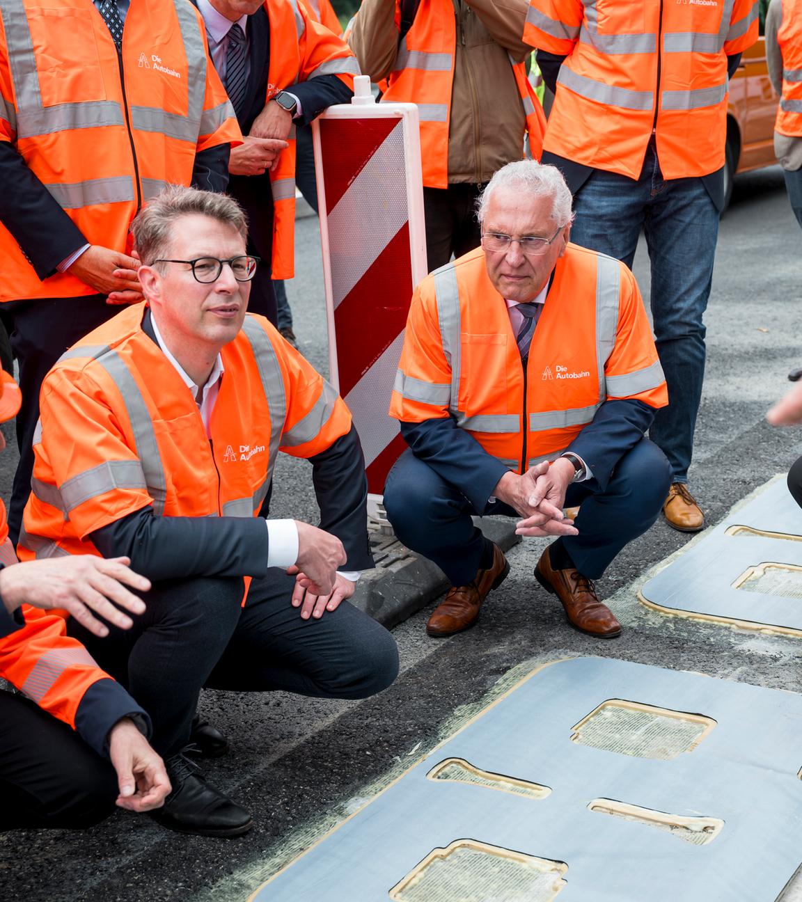 Markus Blume (CSU, 2.v.l), Bayerischer Wissenschaftsminister, und Joachim Herrmann (CSU, M), Bayerischer Innenminister, lassen sich die Funktionsweise des induktiven Ladens auf der A6 erklären. 