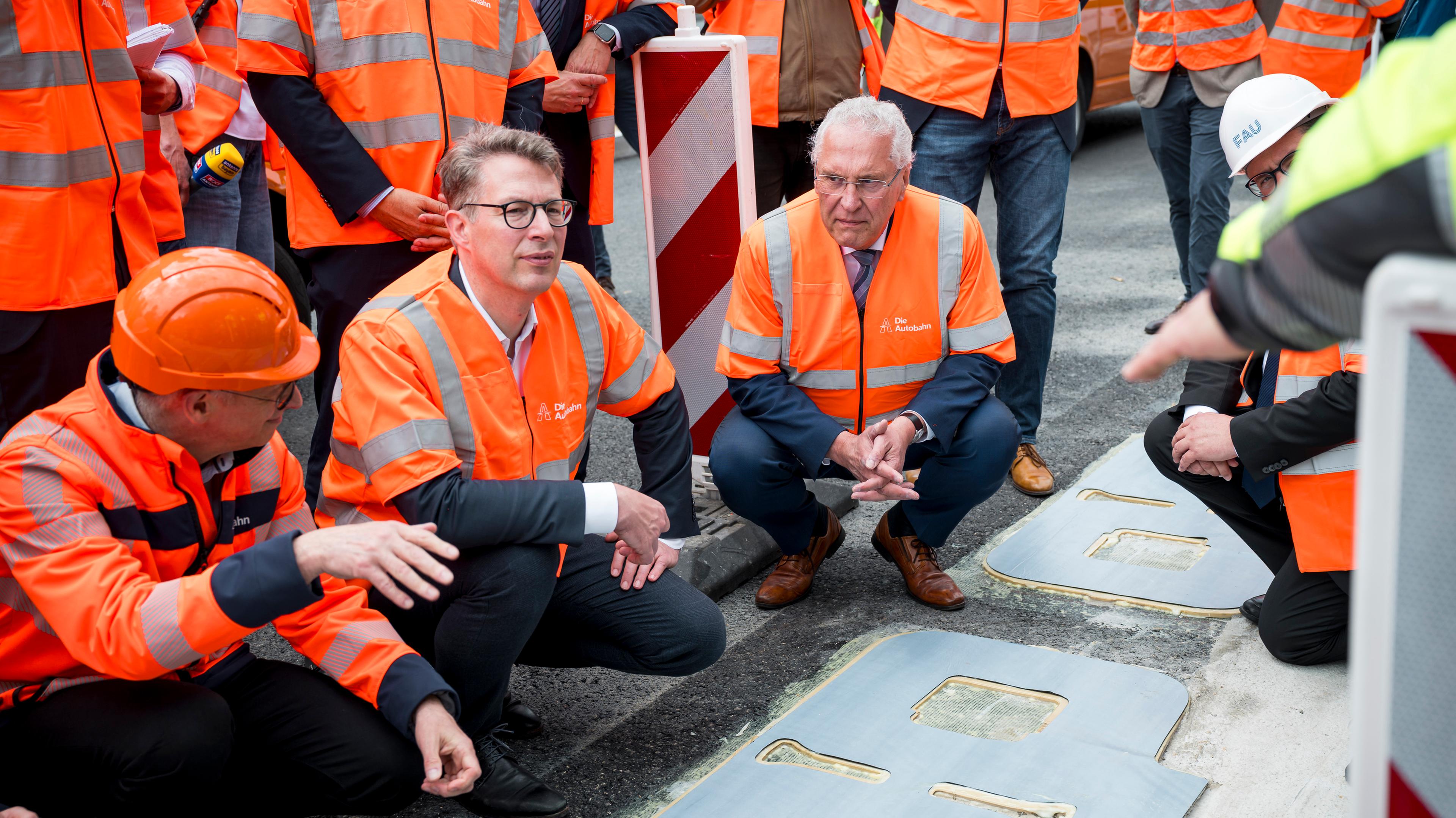 Markus Blume (CSU, 2.v.l.), Bayerischer Wissenschaftsminister, und Joachim Herrmann (CSU, M.), Bayerischer Innenminister, lassen sich die Funktionsweise des induktiven Ladens auf der A6 erklären. 