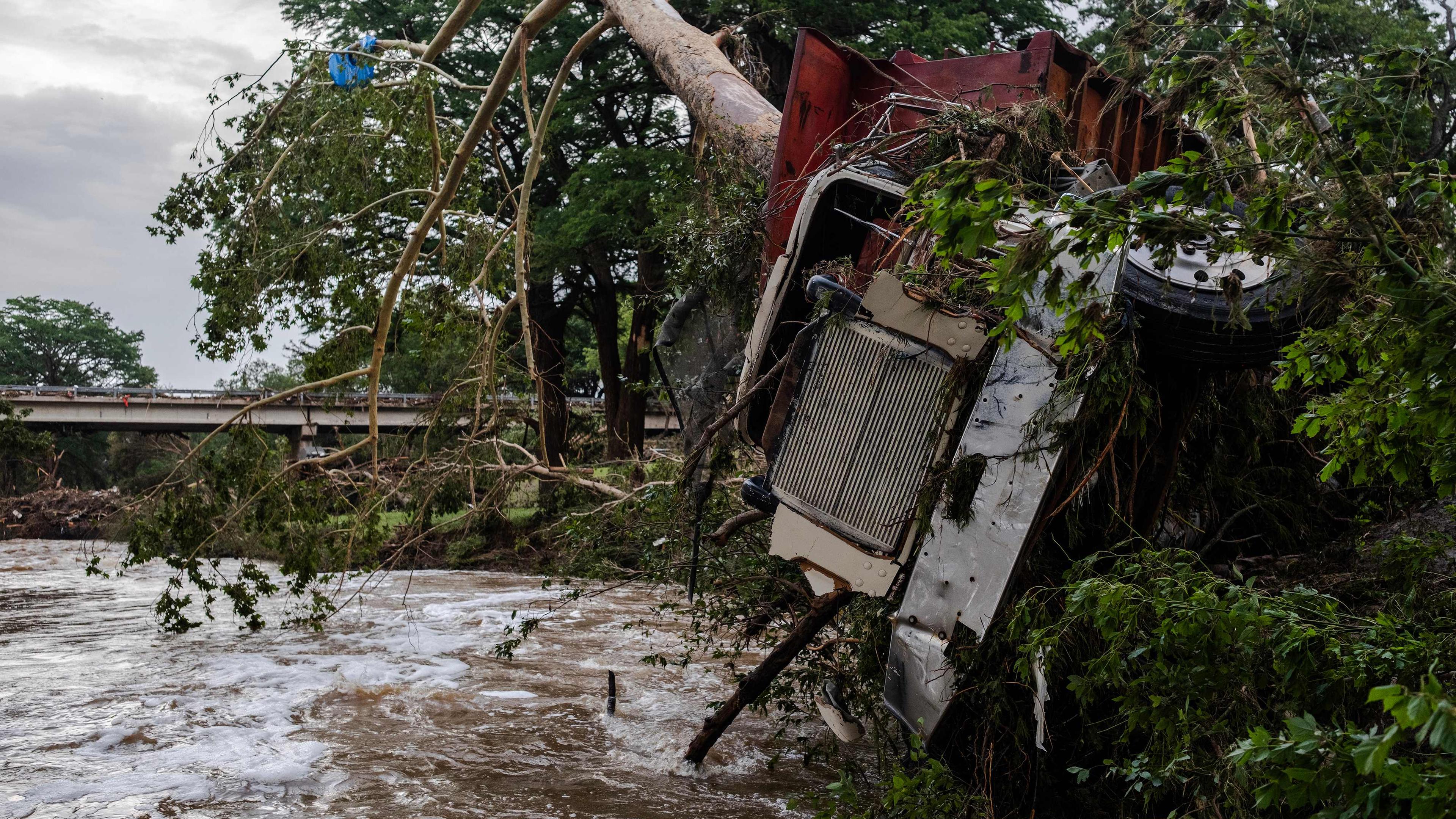 Ein Lkw liegt zerstört neben einem Fluss. Ein Baum steckt in den Fahrzeug