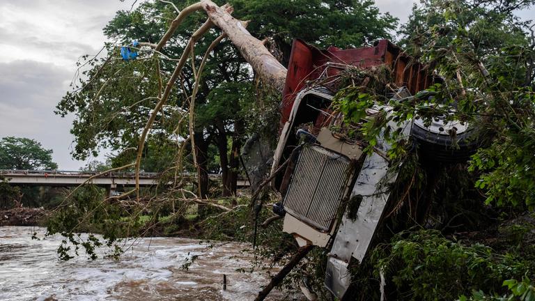 Ein Lkw liegt zerstört neben einem Fluss. Ein Baum steckt in den Fahrzeug
