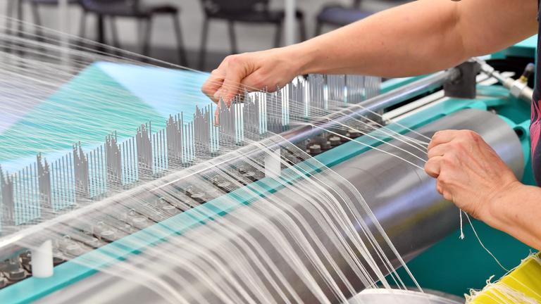 Eine Mitarbeiterin bestückt in einer Textilweberei die sogenannte "Zettelmaschine" mit Garn.