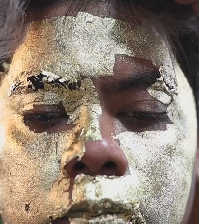 Ein Mann bekommt Blattgold auf sein Gesicht geklebt