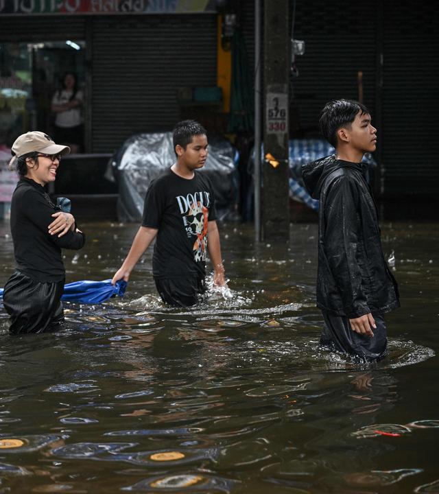 Vier junge Männer laufen durch eine überschwemmte Straße, das Wasser steht ihnen fast bis zum Bauch.