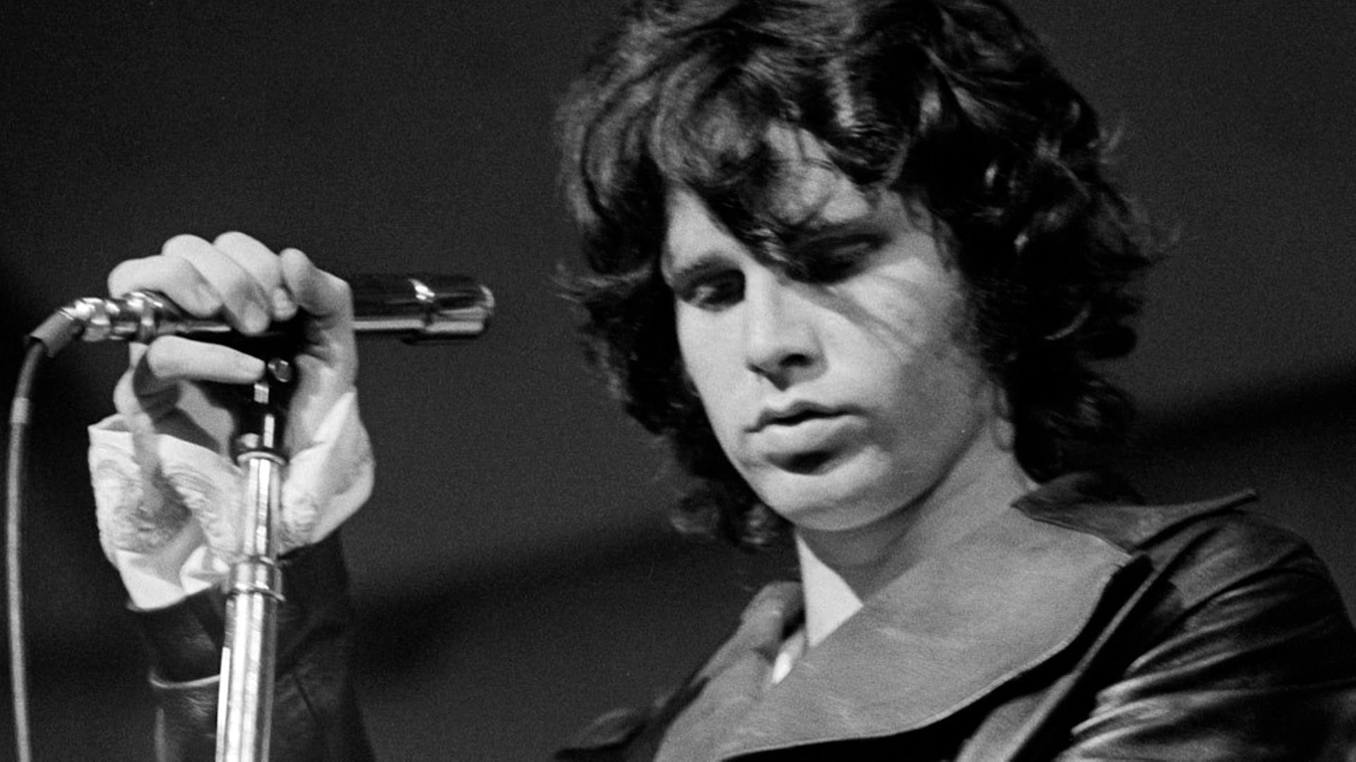 Schwarz-Weiß-Foto von Jim Morrison bei einem Konzert. Er hält das Mikro in der Hand und hat die Augen geschlossen.
