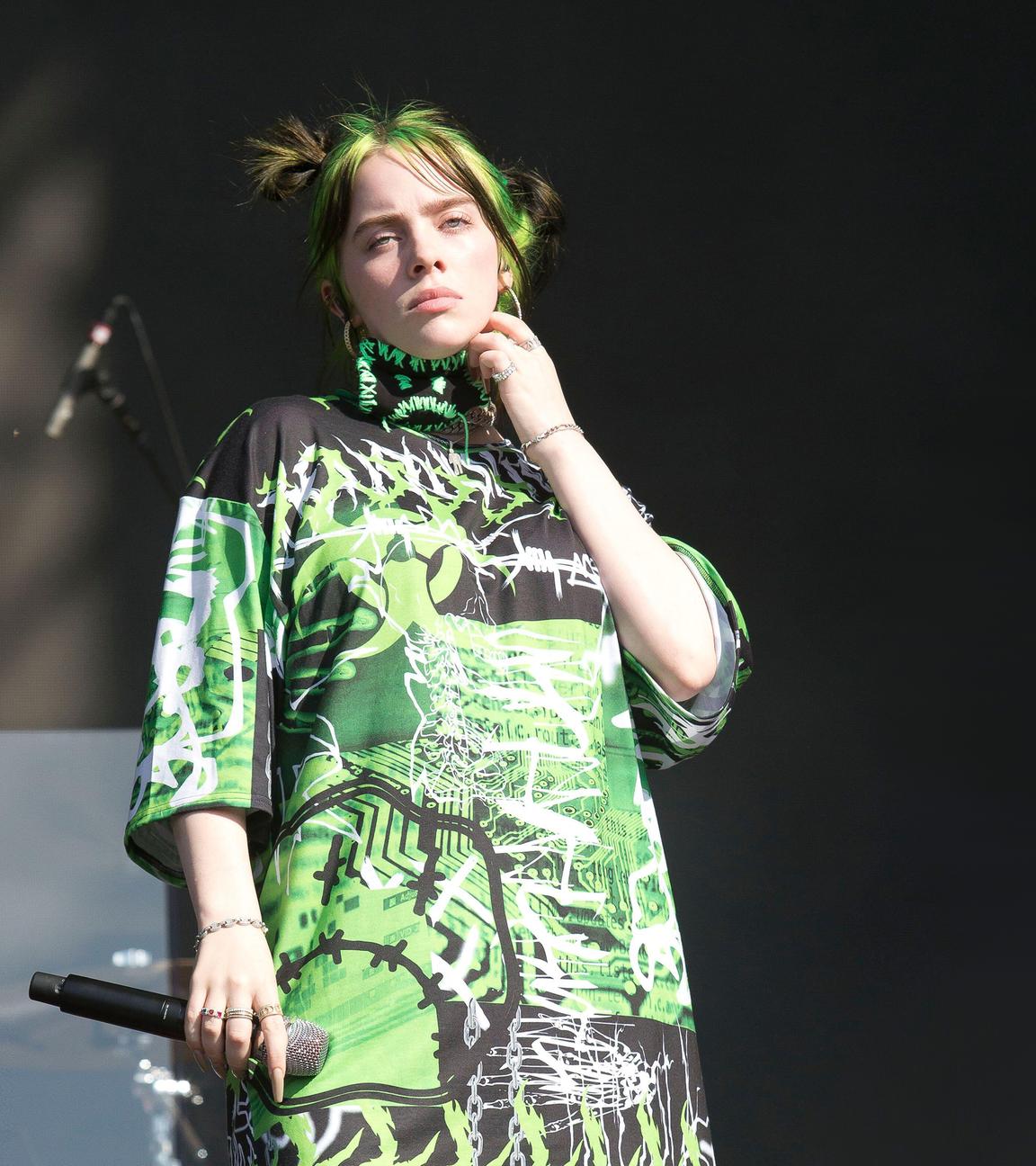 Billie Eilish mit einem Mikro in der Hand schaut Ernst von einer Bühne runter.