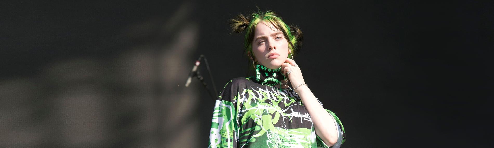 Billie Eilish mit einem Mikro in der Hand schaut Ernst von einer Bühne runter.