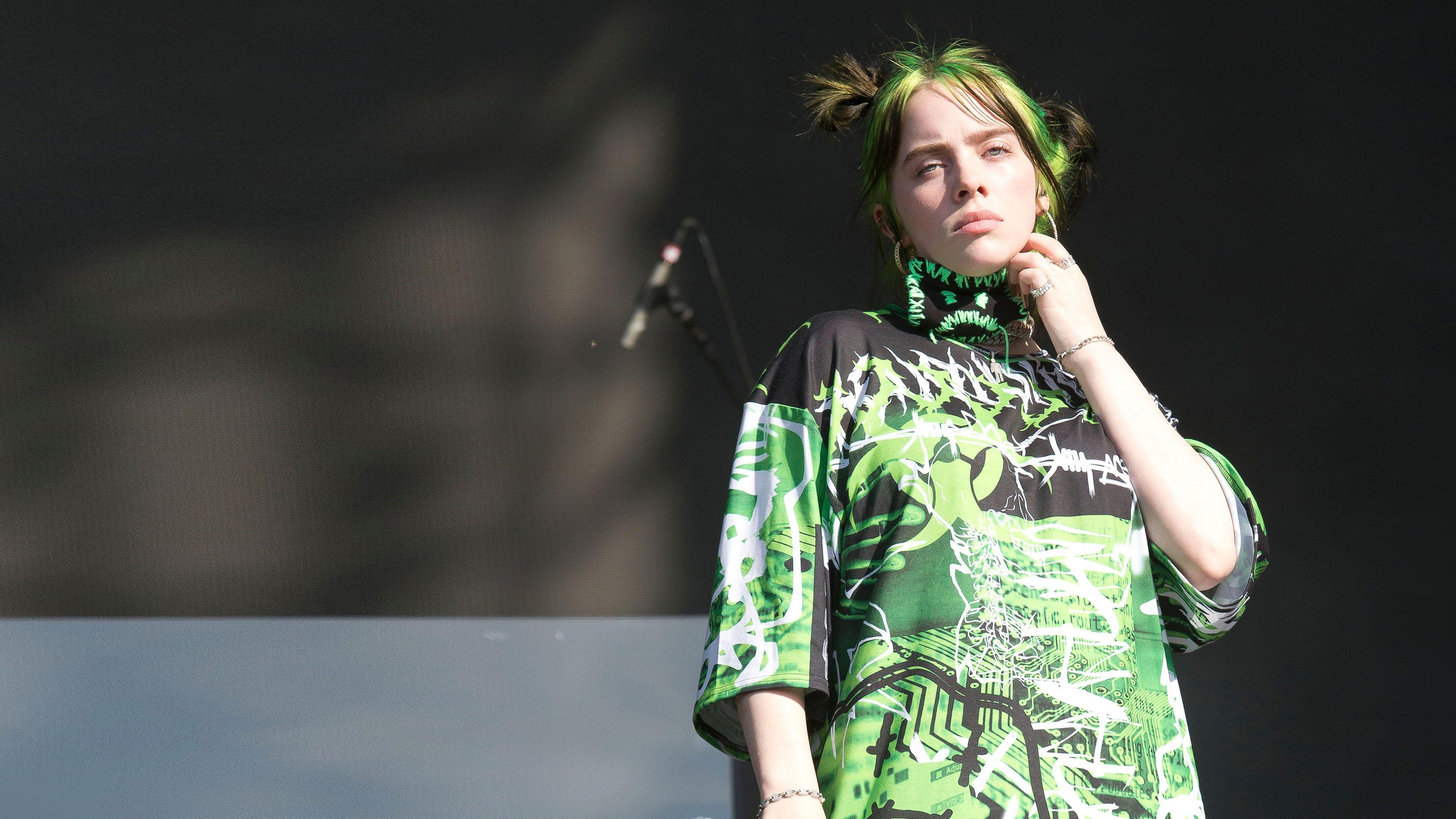 Billie Eilish mit einem Mikro in der Hand schaut Ernst von einer Bühne runter.