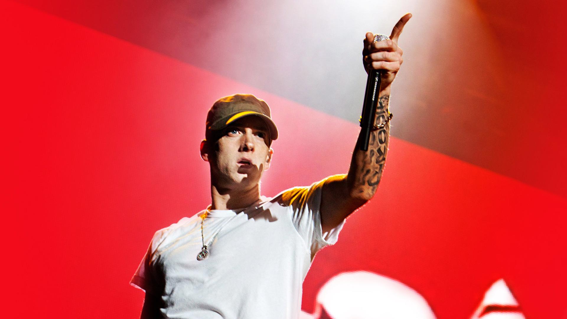 Eminem in einem weißen T-shirt vor einem roten Hintergrund.