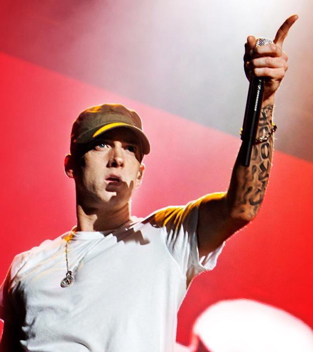 Eminem in einem weißen T-shirt vor einem roten Hintergrund.