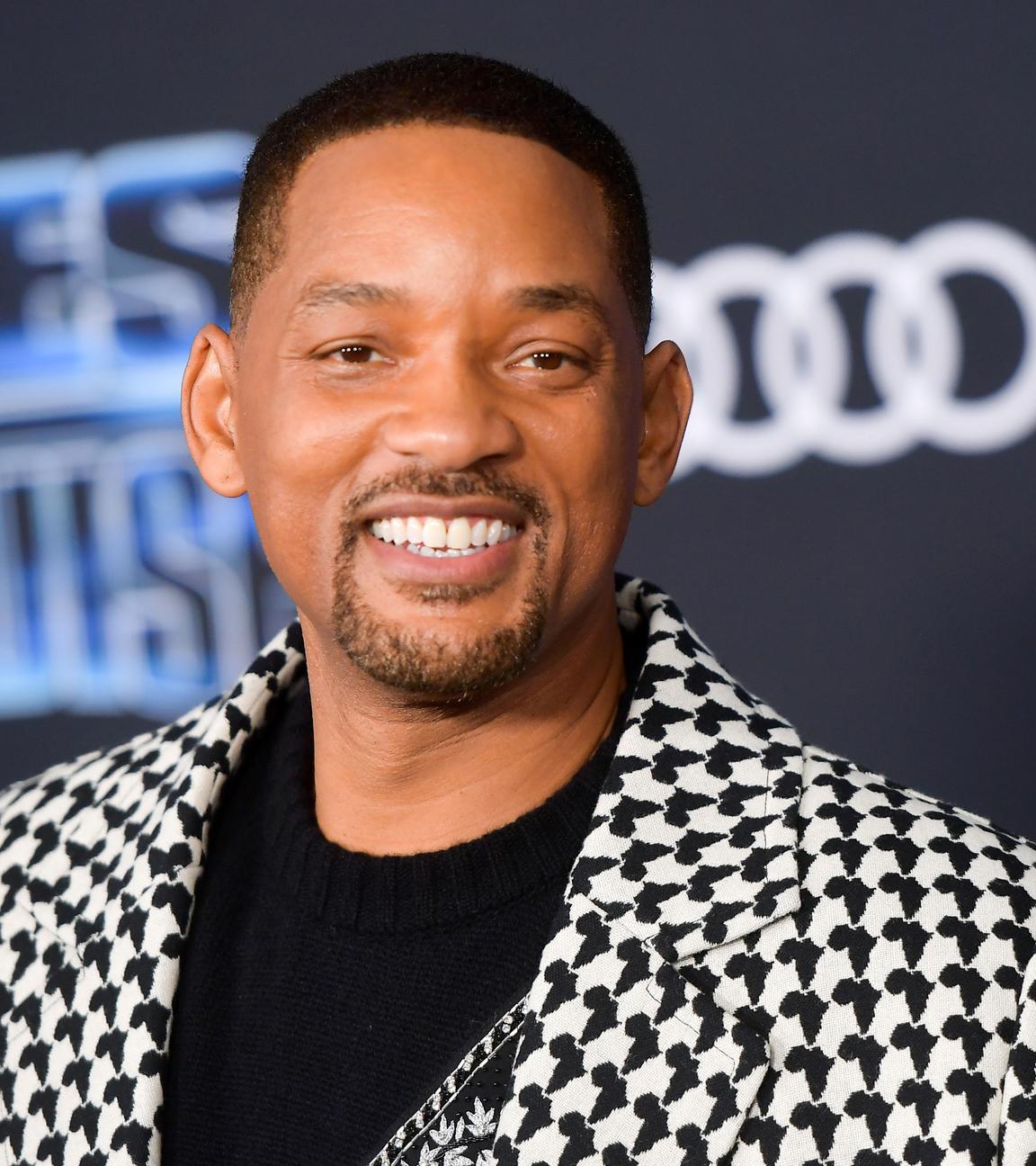 Nahaufnahme von Will Smith. Er trägt ein Hahnentritt-Sakko und lächelt in die Kamera.